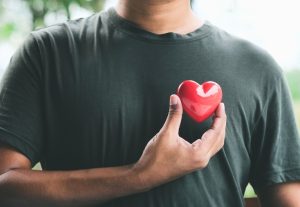 Man holding a red heart against his chest.