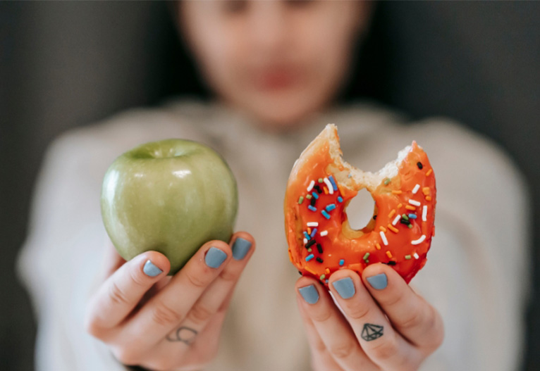 Person holding up an apple and a doughnut.