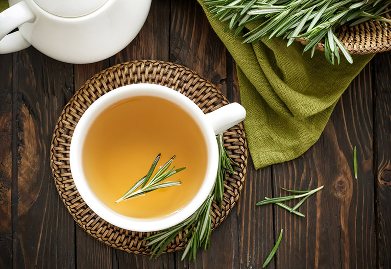Mug of herbal tea with a sprig of rosemary in it.