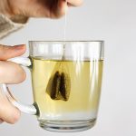 Person holding a mug of tea with a tea bag in it.