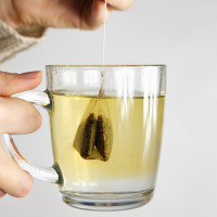 Person holding a mug of tea with a tea bag in it.