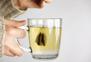 Person holding a mug of tea with a tea bag in it.
