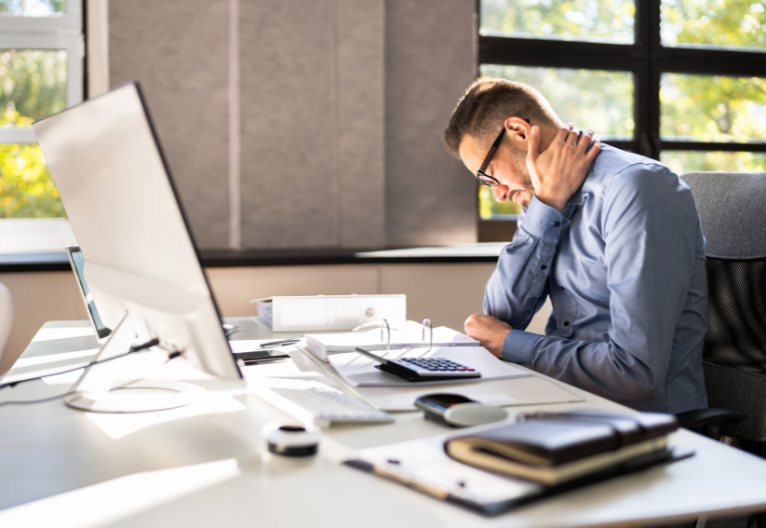 Man at a desk holding his neck.