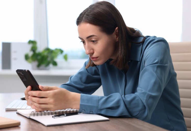 Woman slouching over her phone at a desk.