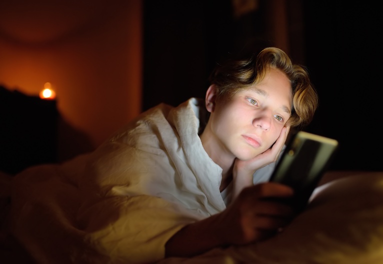 Unhappy teenage boy on his phone in the dark.
