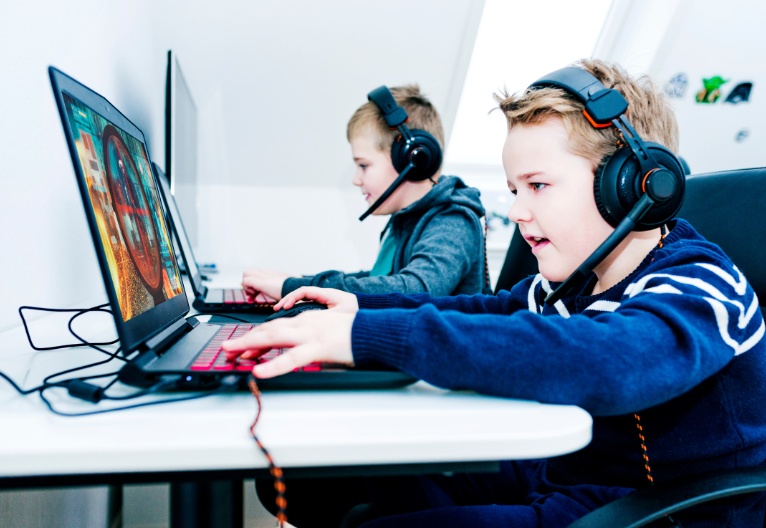 Two boys gaming on computers at a desk.