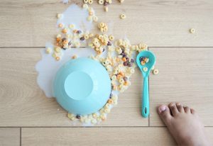 Child's foot next to spilled cereal on a floor.