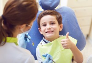 Smiling child with his thumb up in the dentist chair.