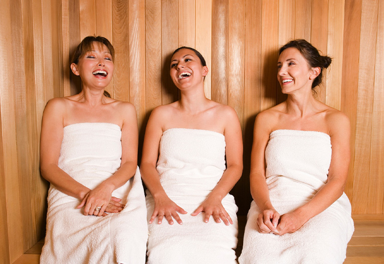 Three women sitting in a sauna laughing.