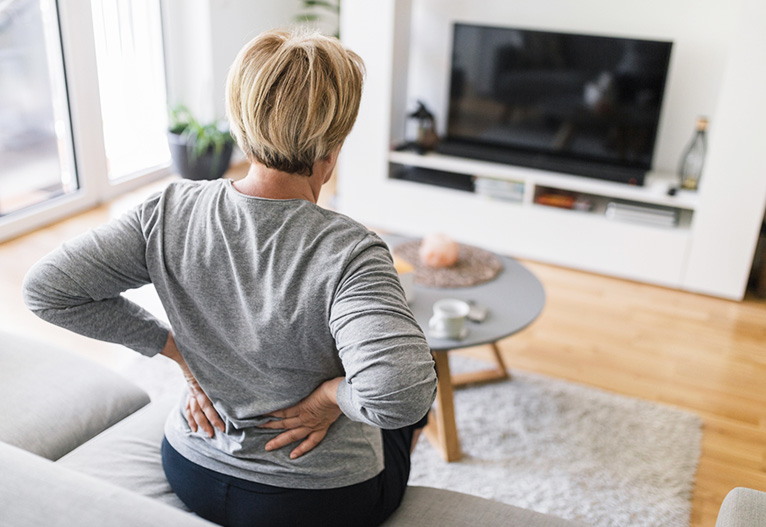 Woman holding her lower back while sitting on the sofa.