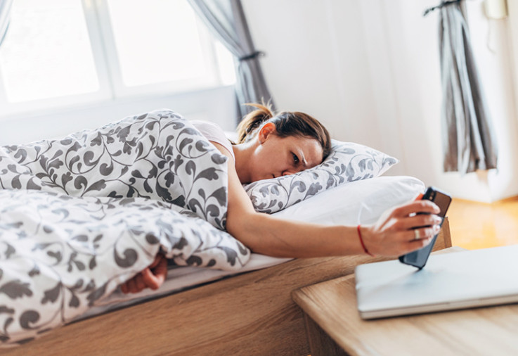 Woman waking up and looking at her phone.