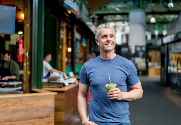 Healthy man walking through city with a green juice.