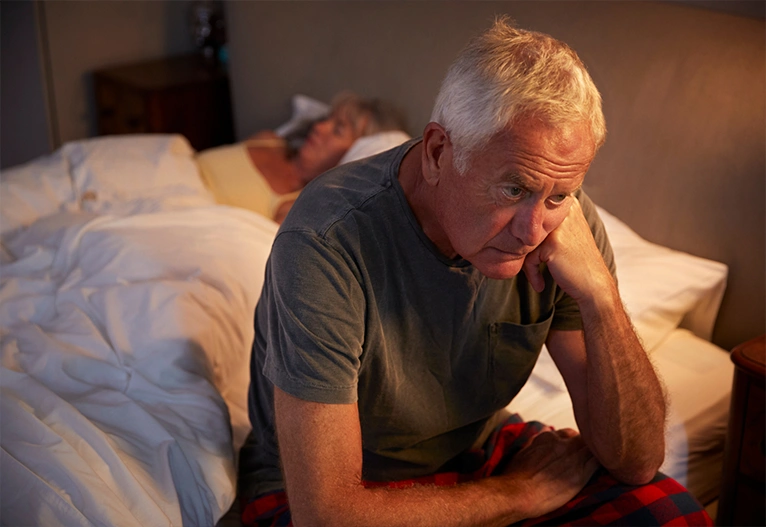 Older man sitting on the edge of his bed unable to sleep.
