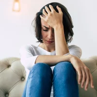 Stressed women sitting on sofa with her head in her hand.