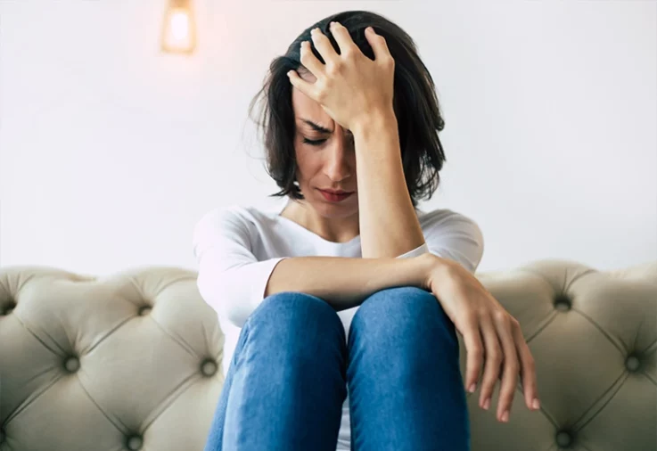 Stressed women sitting on sofa with her head in her hand.