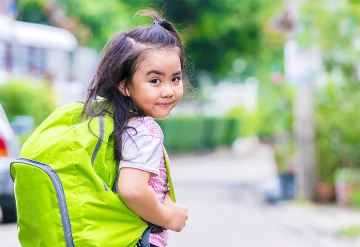 Girl walking to school with a green backpack.