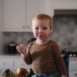 Toddler sitting on a kitchen bench eating a snack.