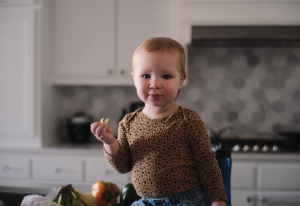 Toddler sitting on a kitchen bench eating a snack.